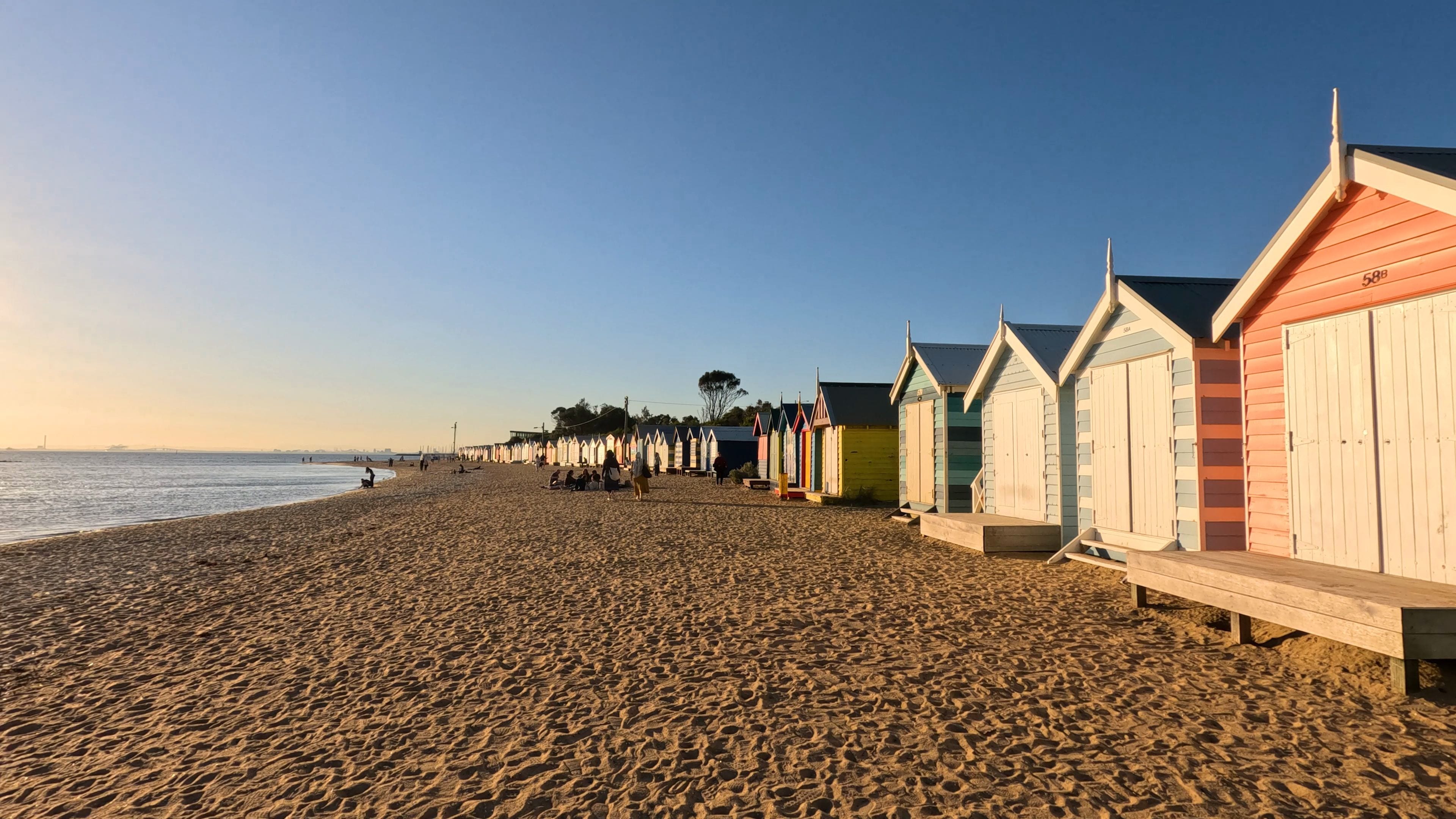 Une plage de sable avec des cabanes de plage aux couleurs vives et un ciel dégagé.