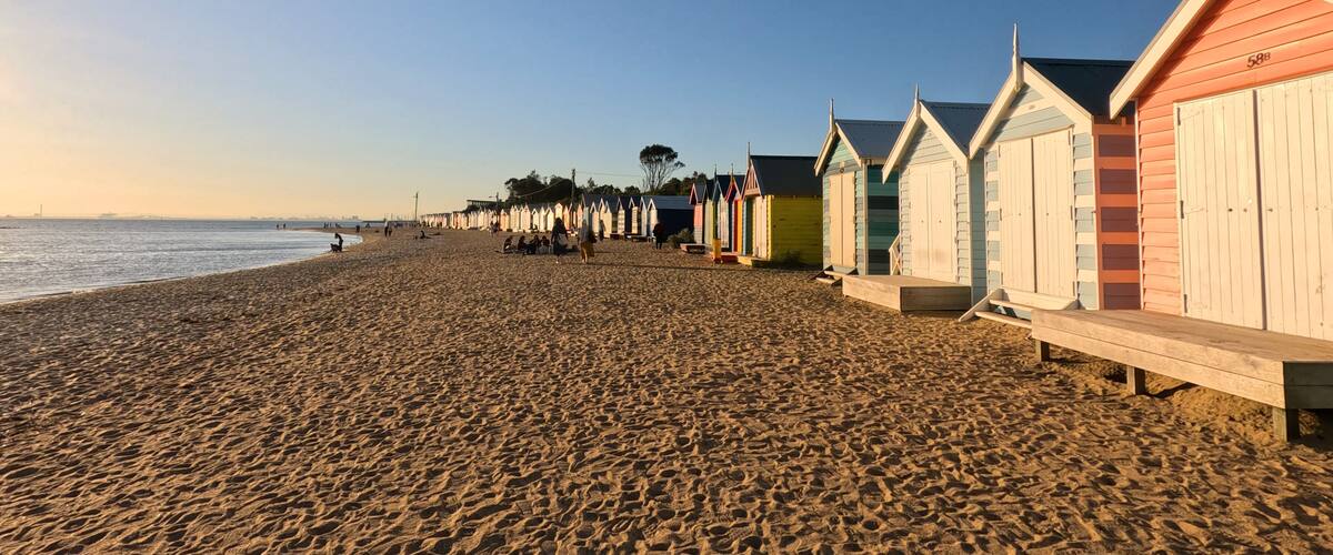 Una playa arenosa con cabañas de playa coloridas y un cielo despejado.