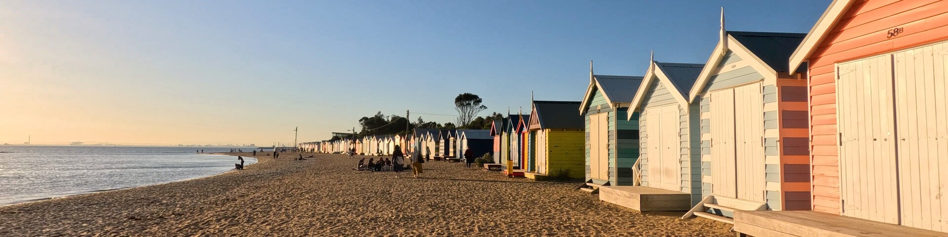 Une plage de sable avec des cabanes de plage aux couleurs vives et un ciel dégagé.