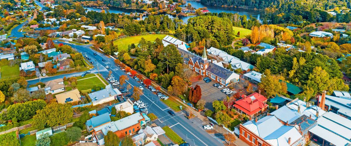 An aerial view of a town with a river, green hills, and autumn-colored trees.