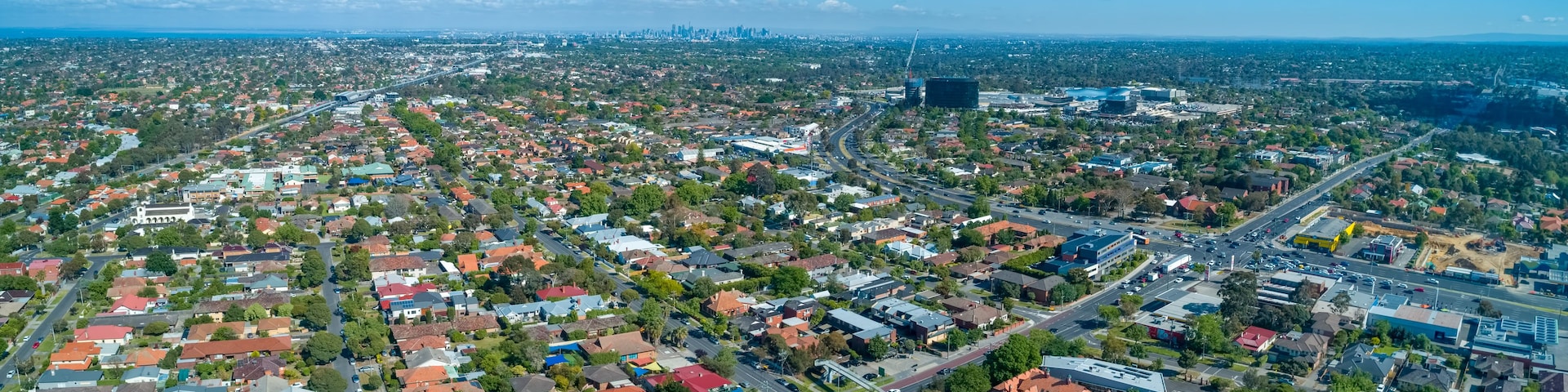 An aerial view of a city with dense residential areas, a large highway, and distant city skyline.
