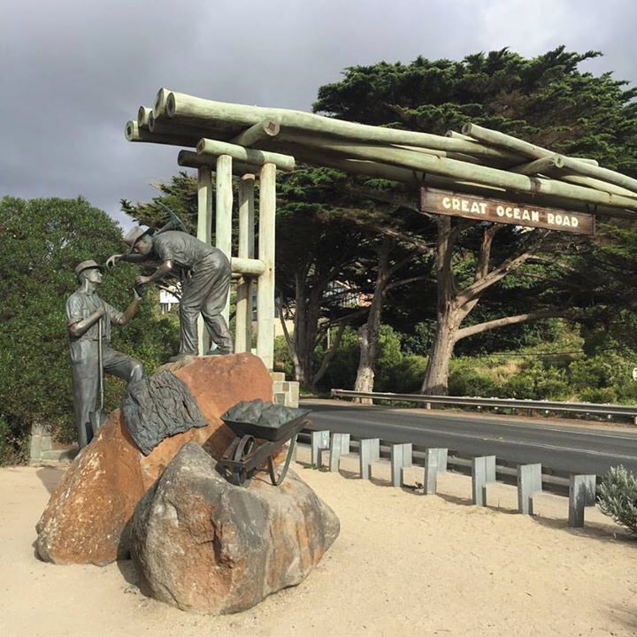 A statue of a man and woman, a wooden structure, and a road sign reading "Great Ocean Road".