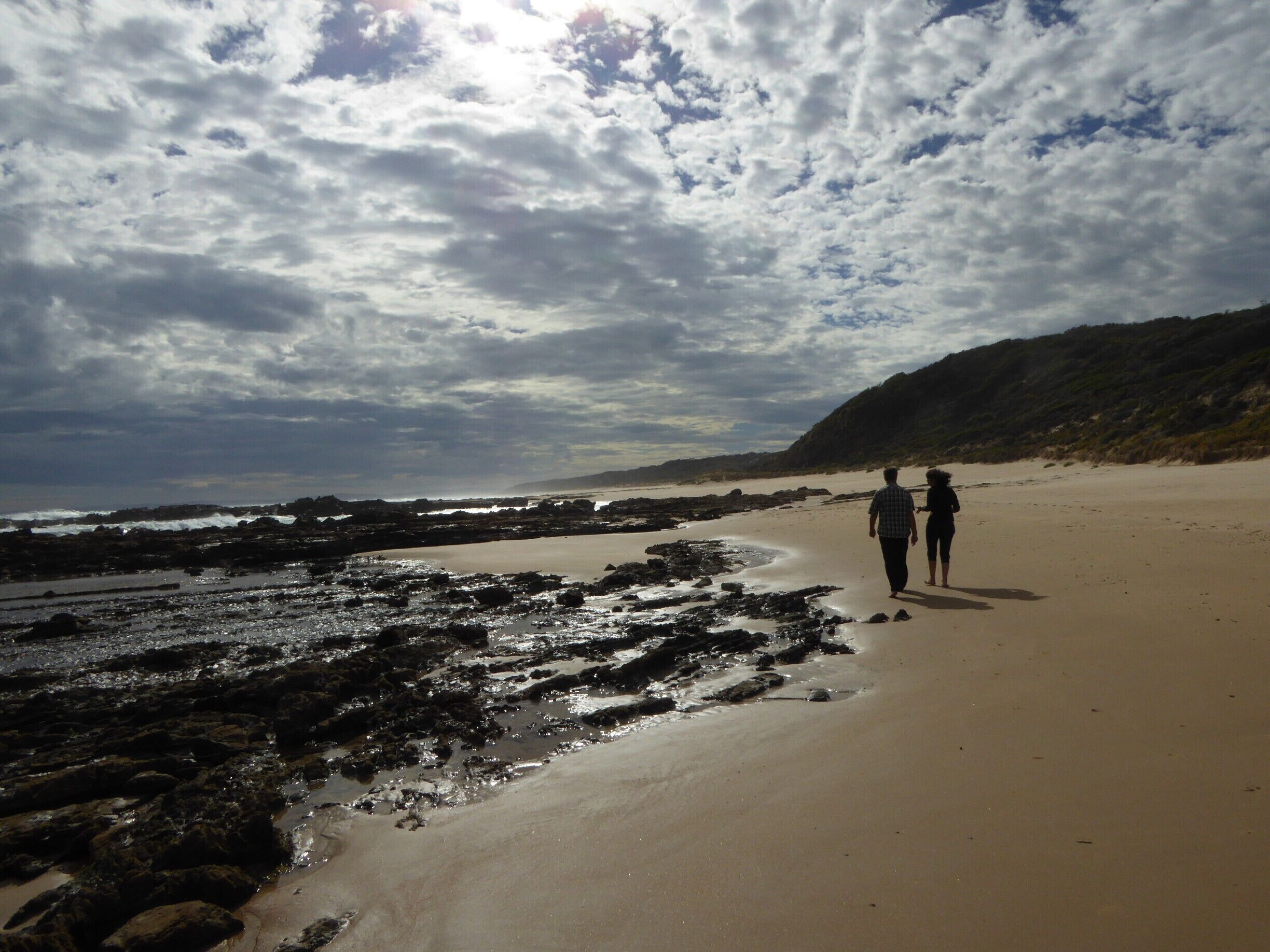 A rocky beach with two people walking along the shore.