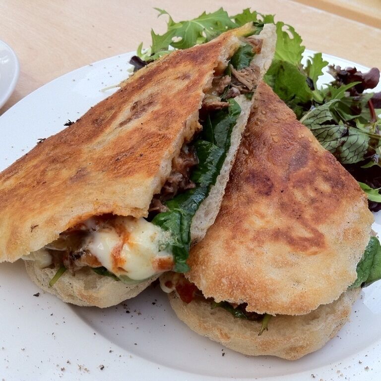 A sandwich with toasted bread, meat, cheese, and greens on a white plate.
