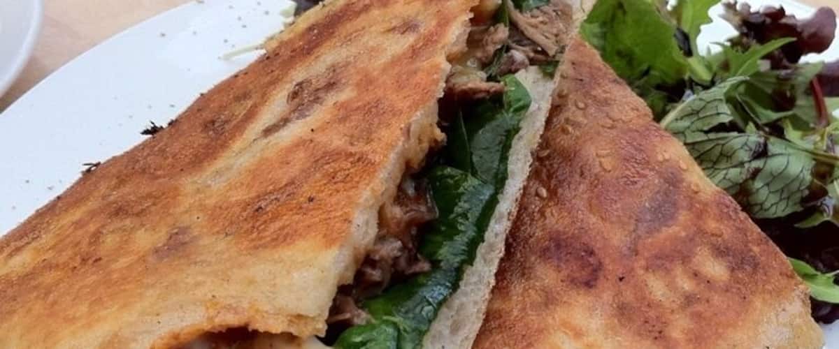 A sandwich with toasted bread, meat, cheese, and greens on a white plate.