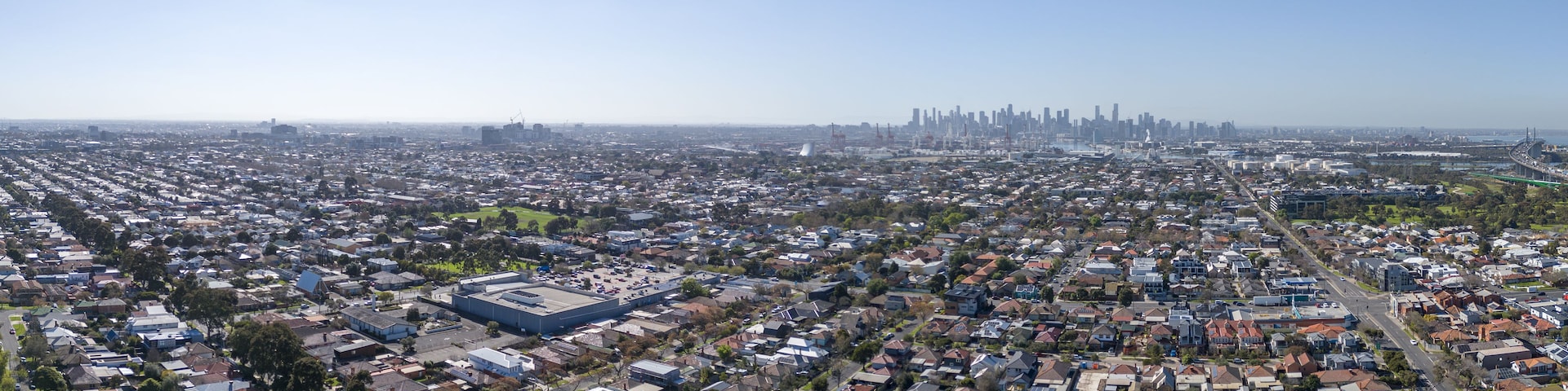 Uma área urbana densamente povoada, com um edifício industrial notável e um horizonte urbano ao longe.