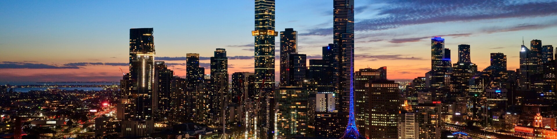 Un horizonte urbano al anochecer con edificios iluminados y una torre destacada.