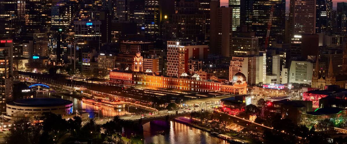 A cityscape at night with illuminated buildings, a river, and a bridge.