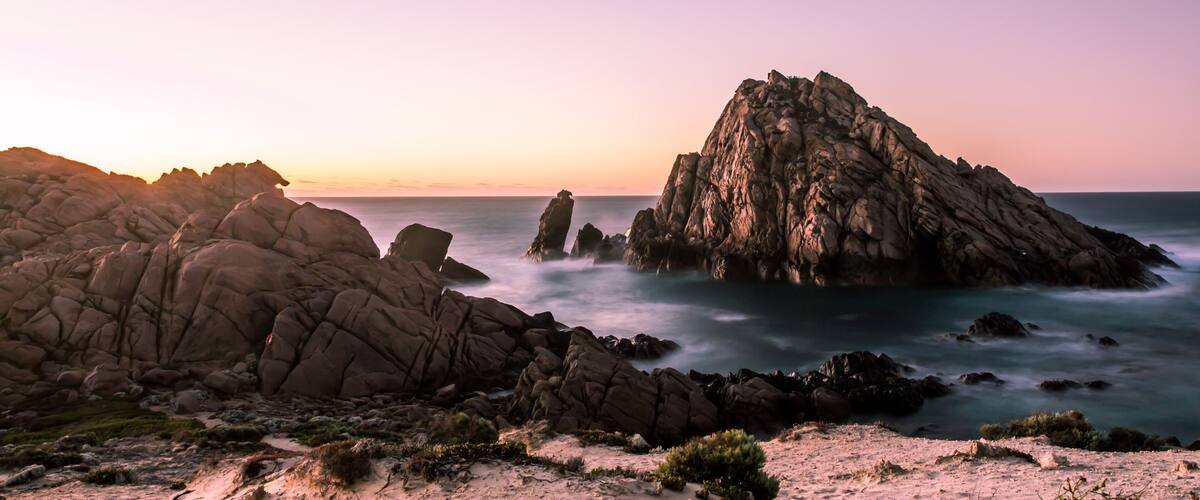 A coastal landscape with prominent rock formations and a calm sea at sunset.