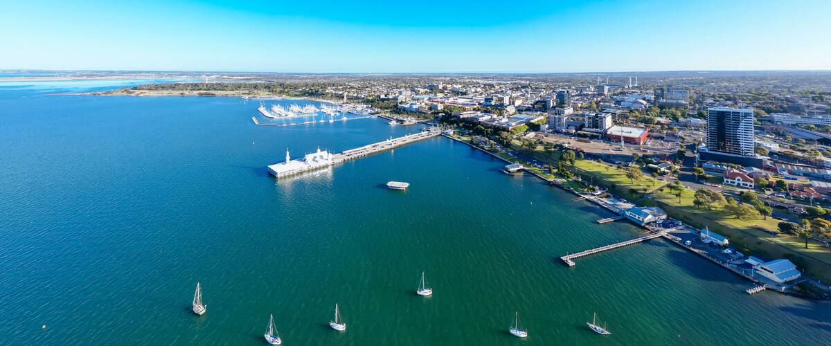A coastal city with a marina, sailboats, and a mix of urban and green spaces.