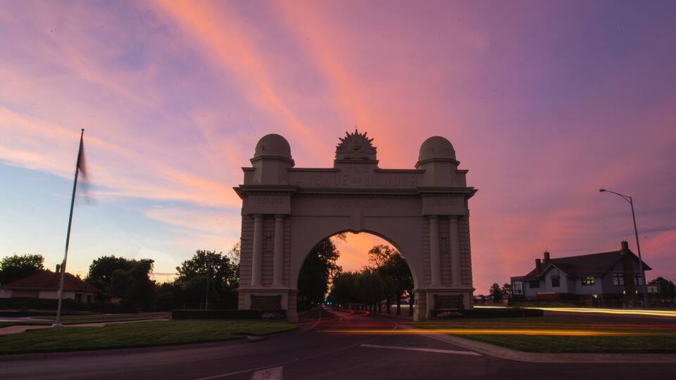 An archway with inscriptions, surrounded by a road and residential houses.