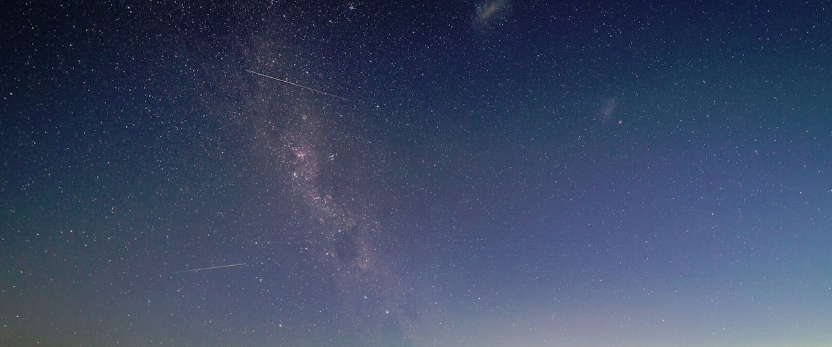 A starry night sky over a calm body of water with a visible Milky Way and city lights in the distance.