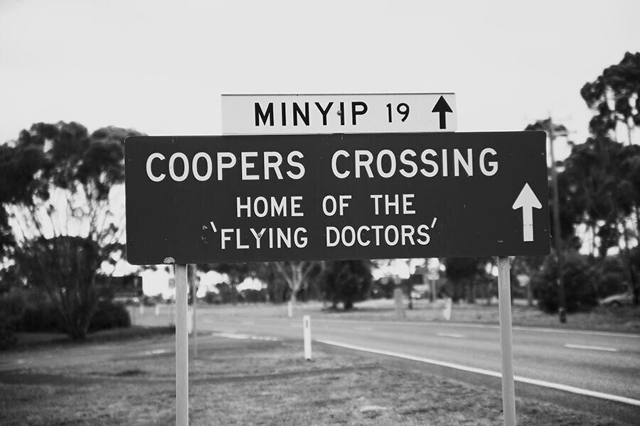 A road sign indicating 'COOPERS CROSSING' and 'HOME OF THE 'FLYING DOCTORS''.