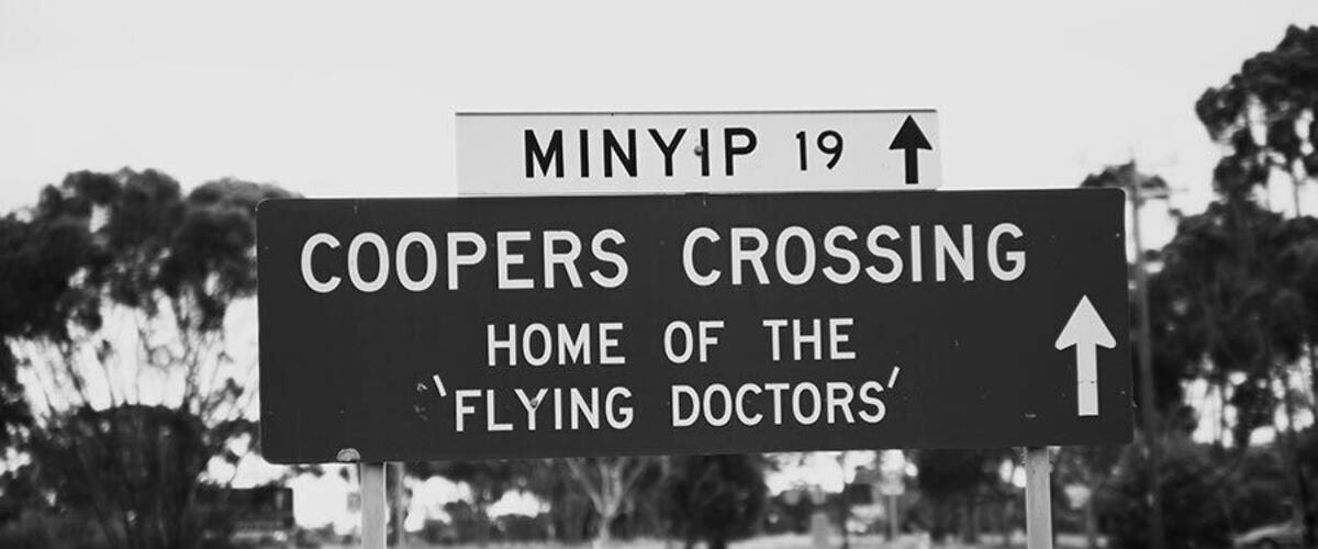 A road sign indicating 'COOPERS CROSSING' and 'HOME OF THE 'FLYING DOCTORS''.