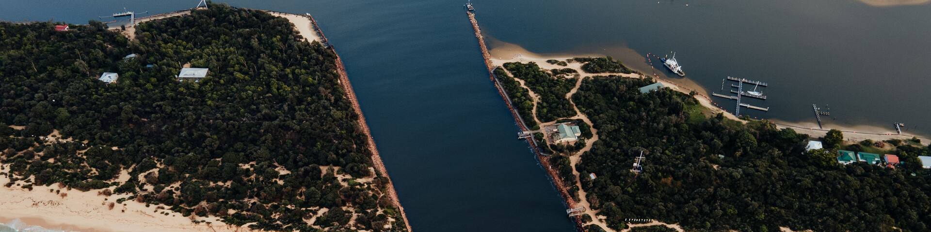 An aerial view of a coastal area with a sandy beach, a narrow waterway, and a dense forested island.