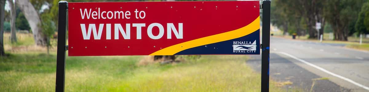 A welcome sign for Winton, Benalla Rural City, with a road and trees in the background.