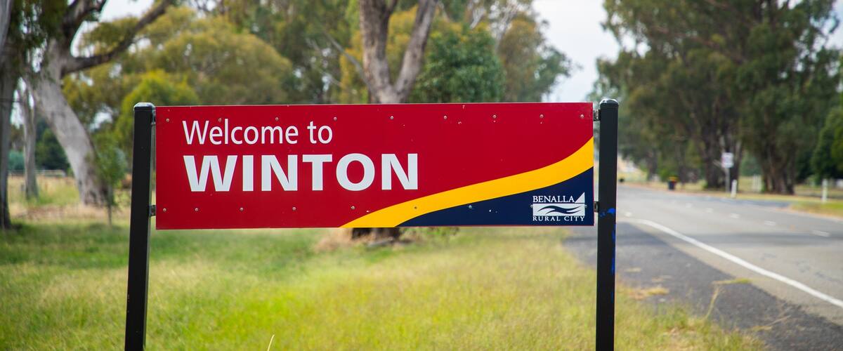 A welcome sign for Winton, Benalla Rural City, with a road and trees in the background.