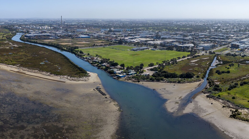 Un paisaje costero con un río, edificios industriales y un campo verde.
