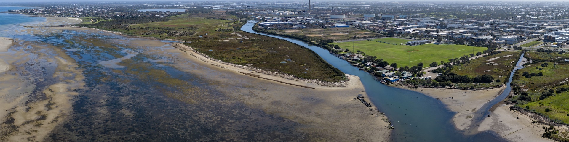 Paisagem costeira com rio, edifícios industriais e um campo verde.