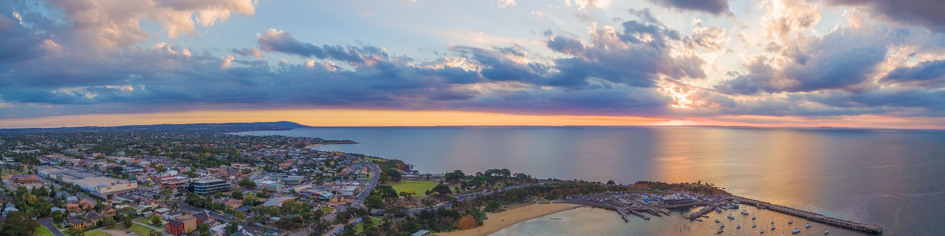 Uma vila costeira com um porto de recreio, praia de areia e um pôr do sol sobre o oceano.