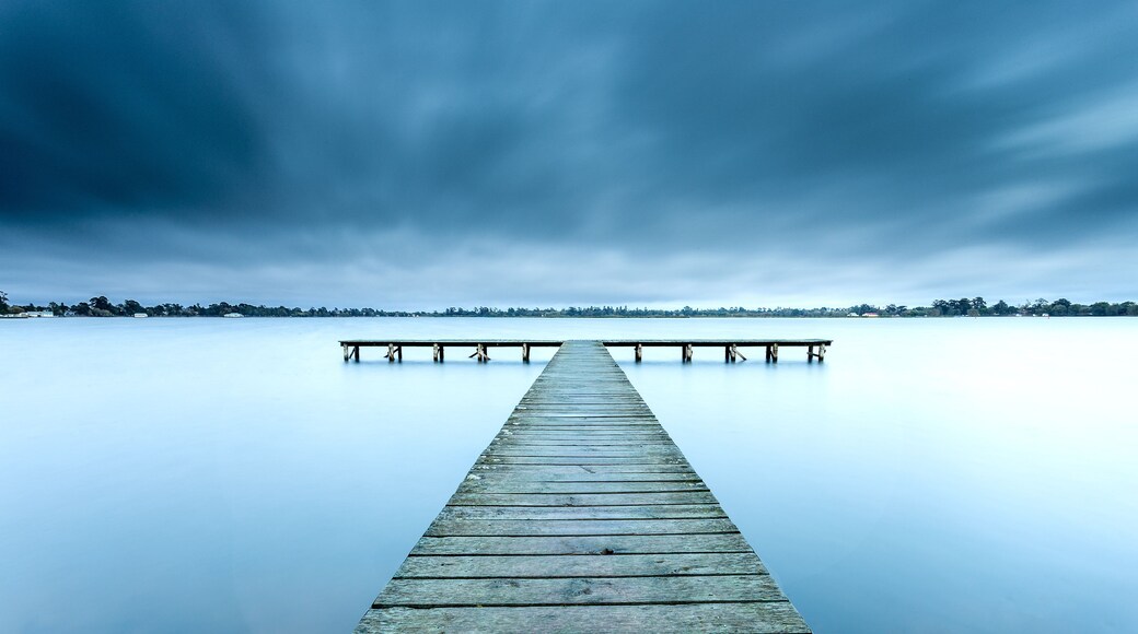 Un muelle de madera que se adentra en aguas tranquilas bajo un cielo nublado.