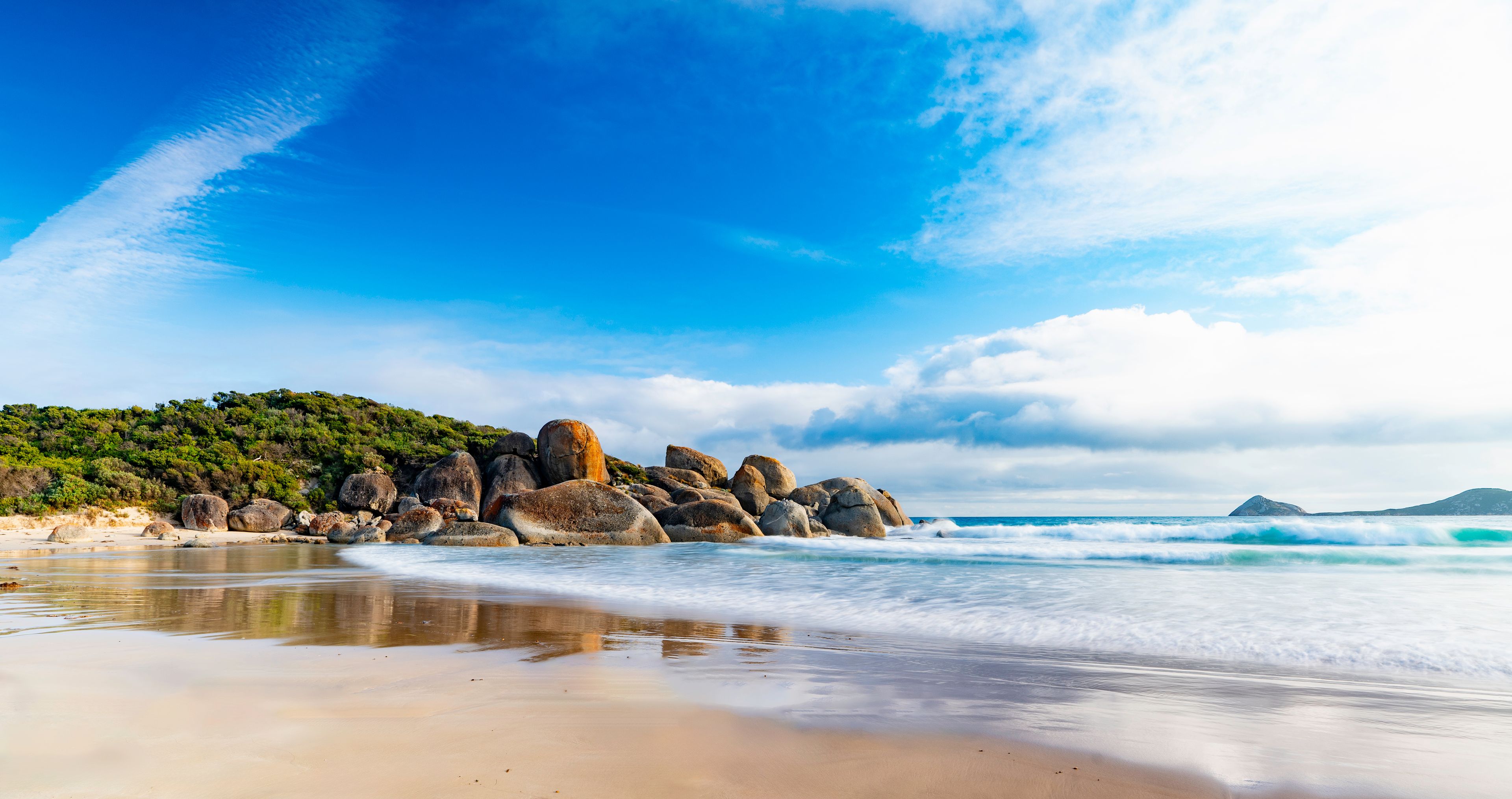 A beach with large rocks, waves, and a clear sky.