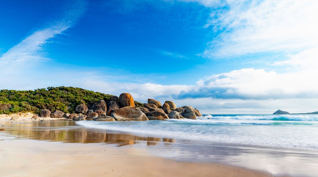 A beach with large rocks, waves, and a clear sky.