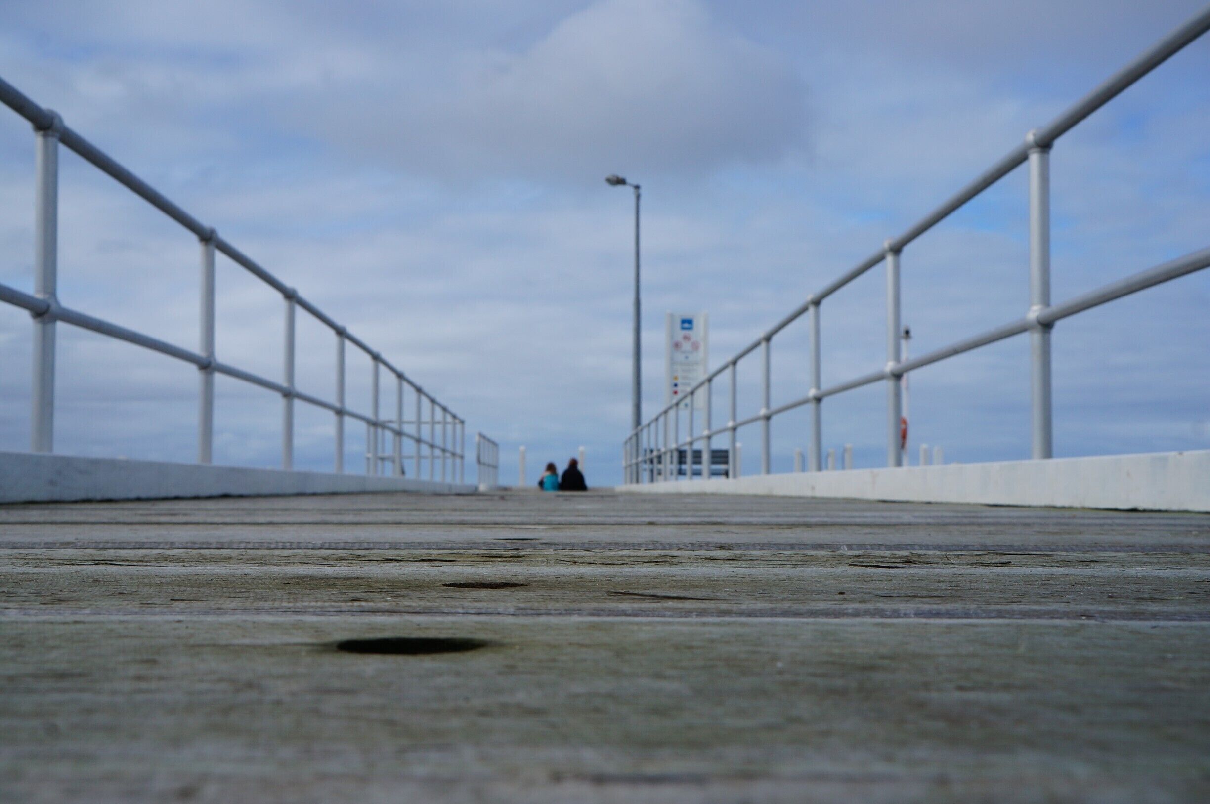 A concrete bridge with metal railings and a street lamp in the distance.