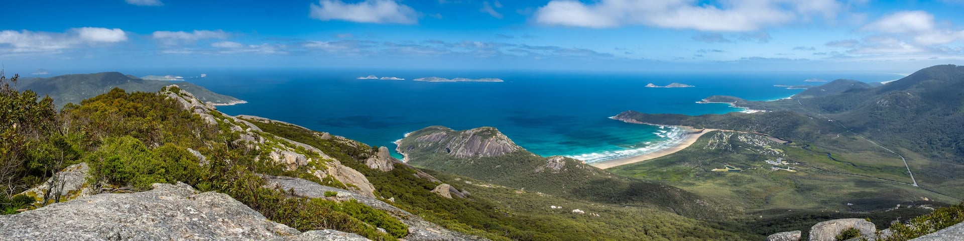 A coastal landscape with mountains, a beach, and clear blue waters.