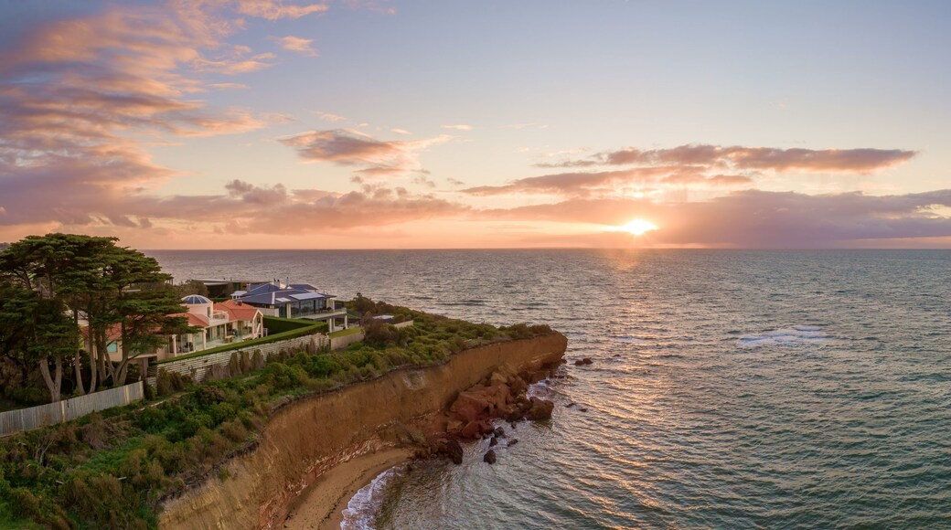Un paysage côtier avec un coucher de soleil, une falaise et une zone résidentielle avec des maisons.