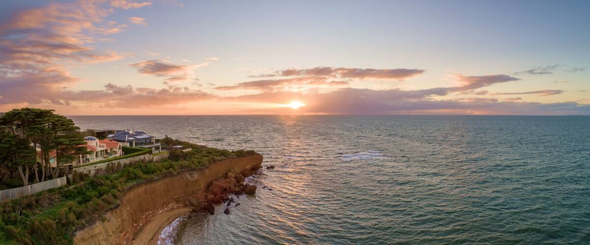 A coastal landscape with a sunset, a cliff, and a residential area with houses.