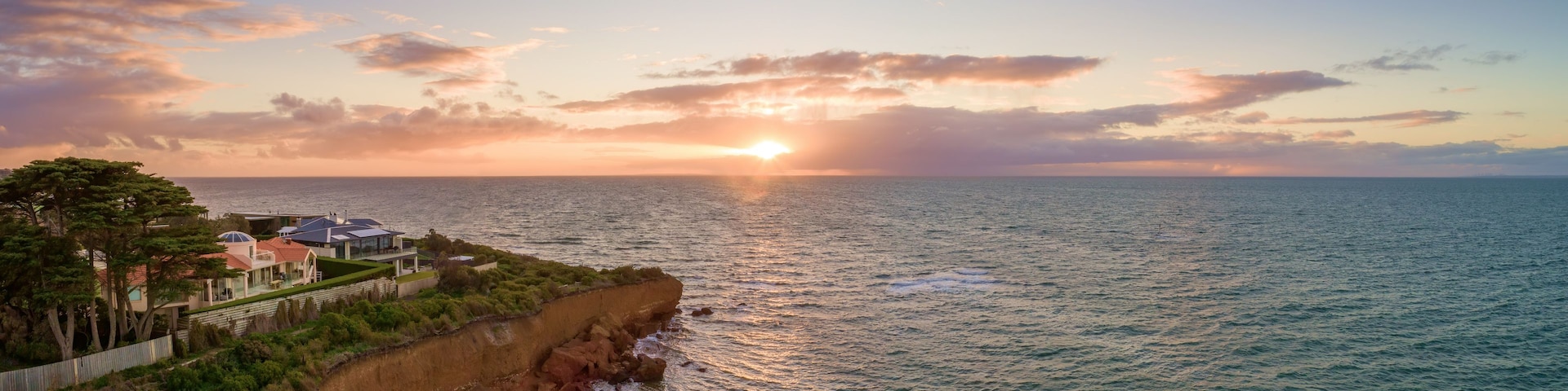 Un paisaje costero con un atardecer, un acantilado y una zona residencial con casas.
