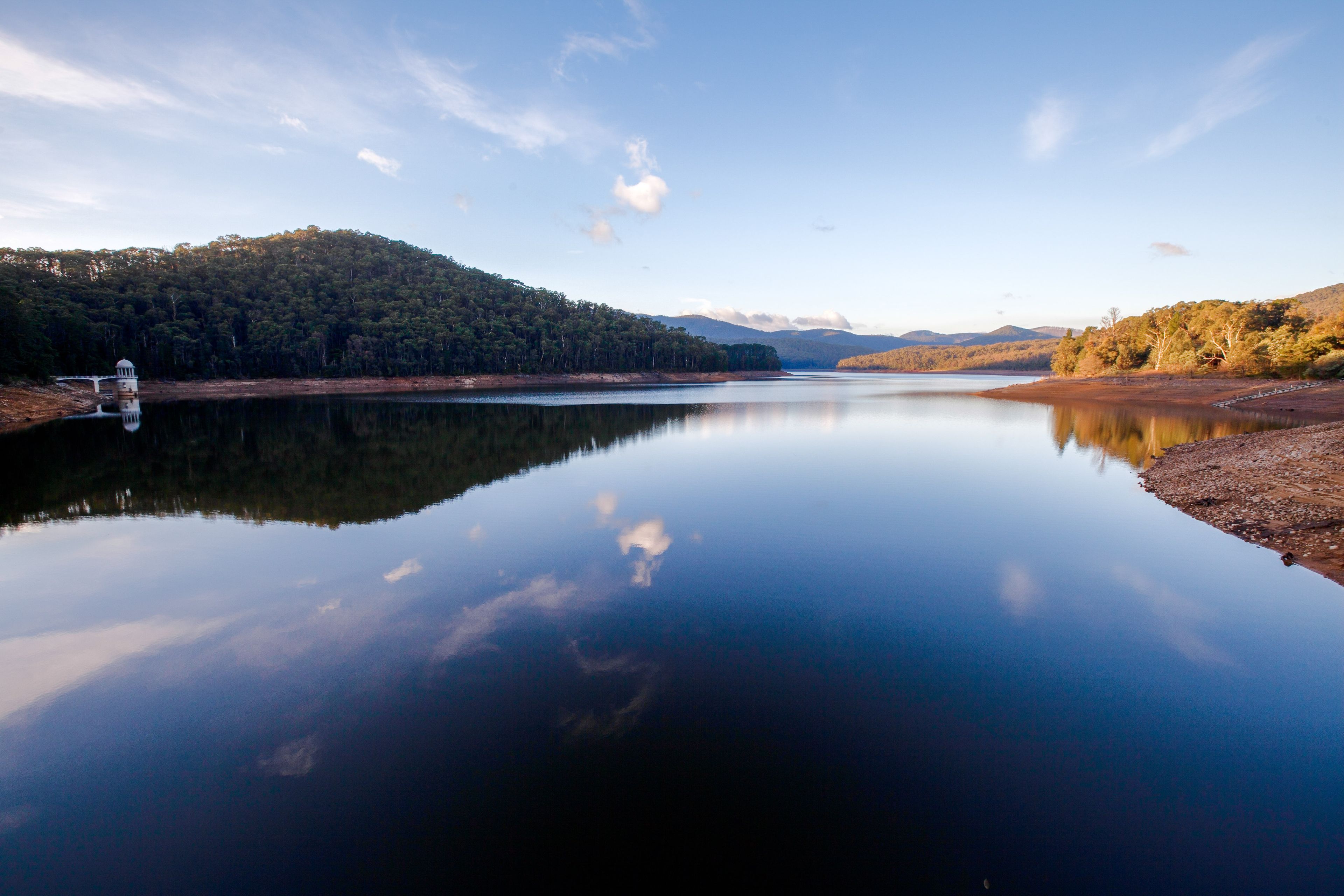 A calm lake with a forested mountain in the background and a small bridge in the foreground.