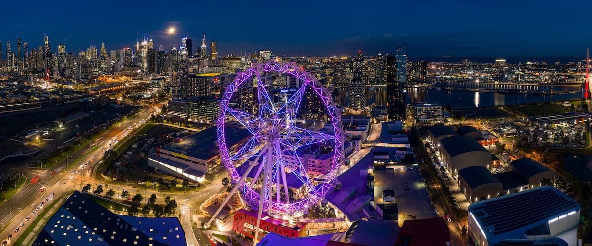 Une vue nocturne d’une ville, avec une grande roue bien visible et un pont.