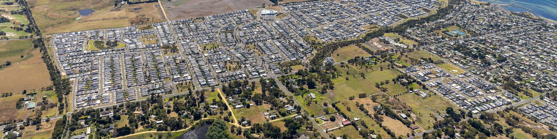 An aerial view of a coastal town with residential areas, a large body of water, and surrounding farmland.