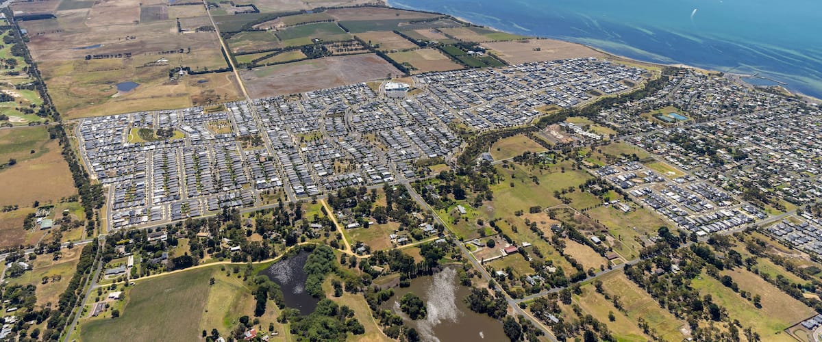 An aerial view of a coastal town with residential areas, a large body of water, and surrounding farmland.