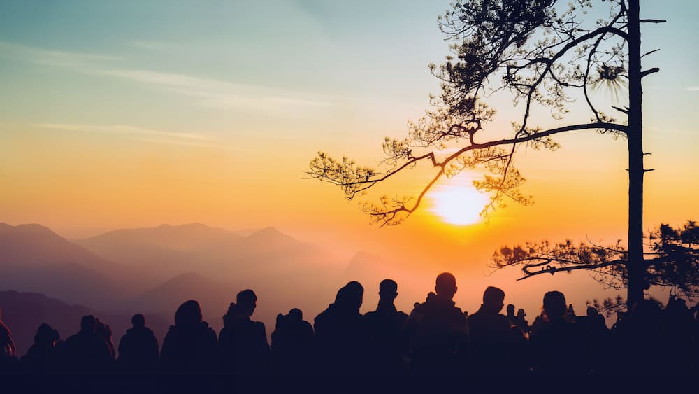 A silhouette of people at sunset with mountains in the background.