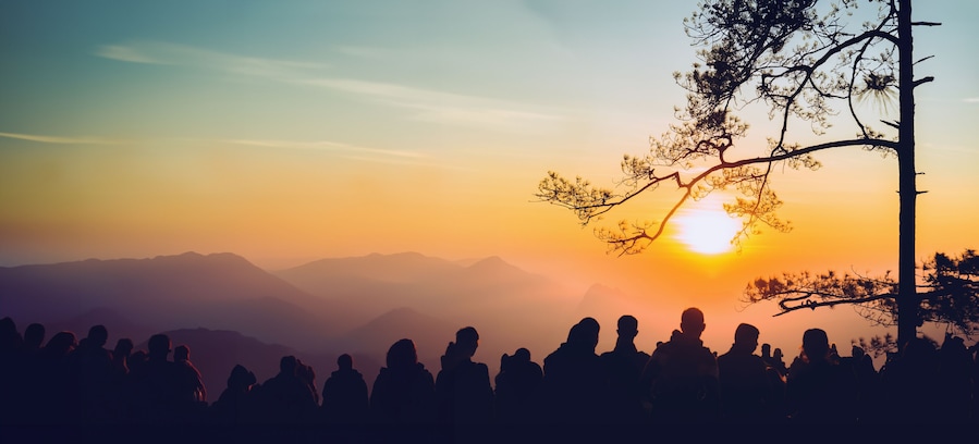 Silueta de personas al atardecer, con montañas al fondo.