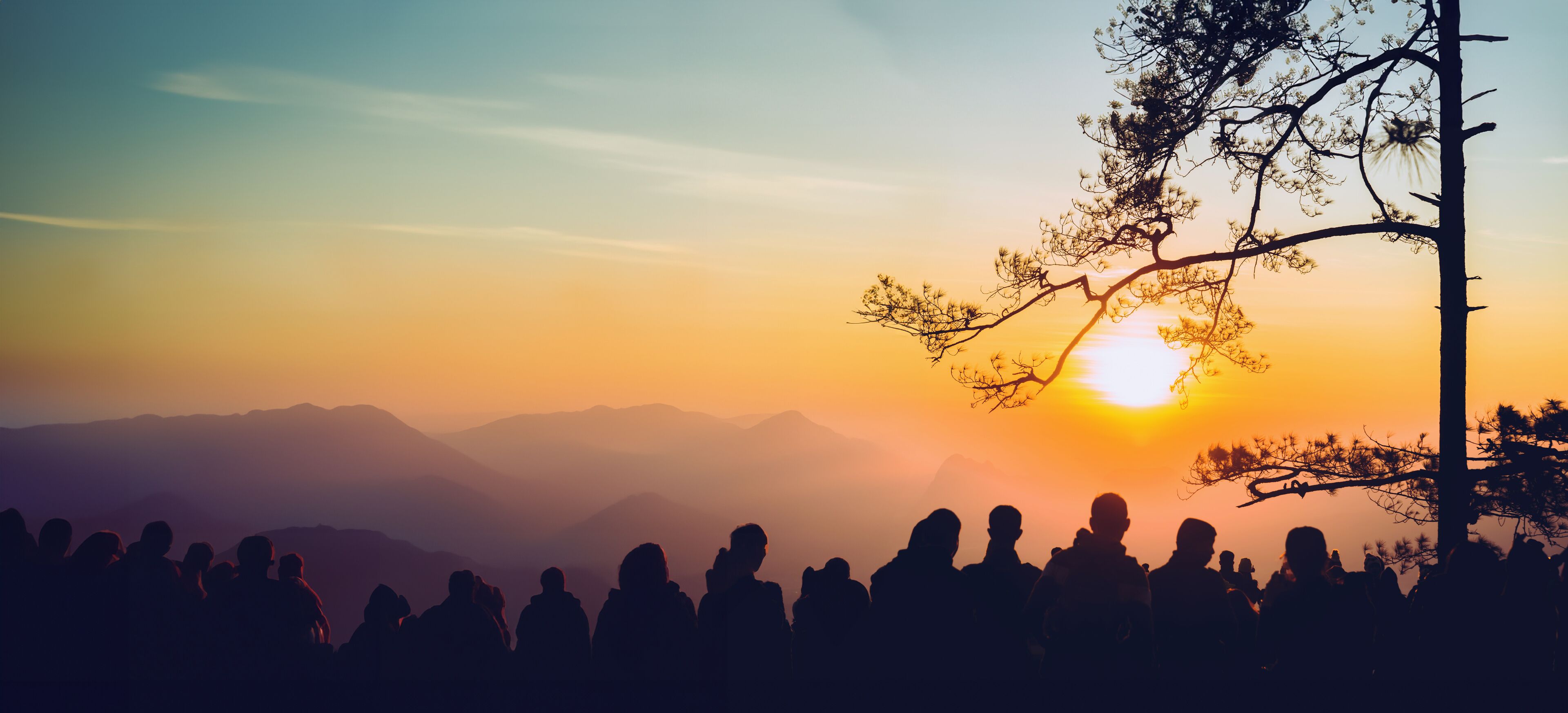 A silhouette of people at sunset with mountains in the background.