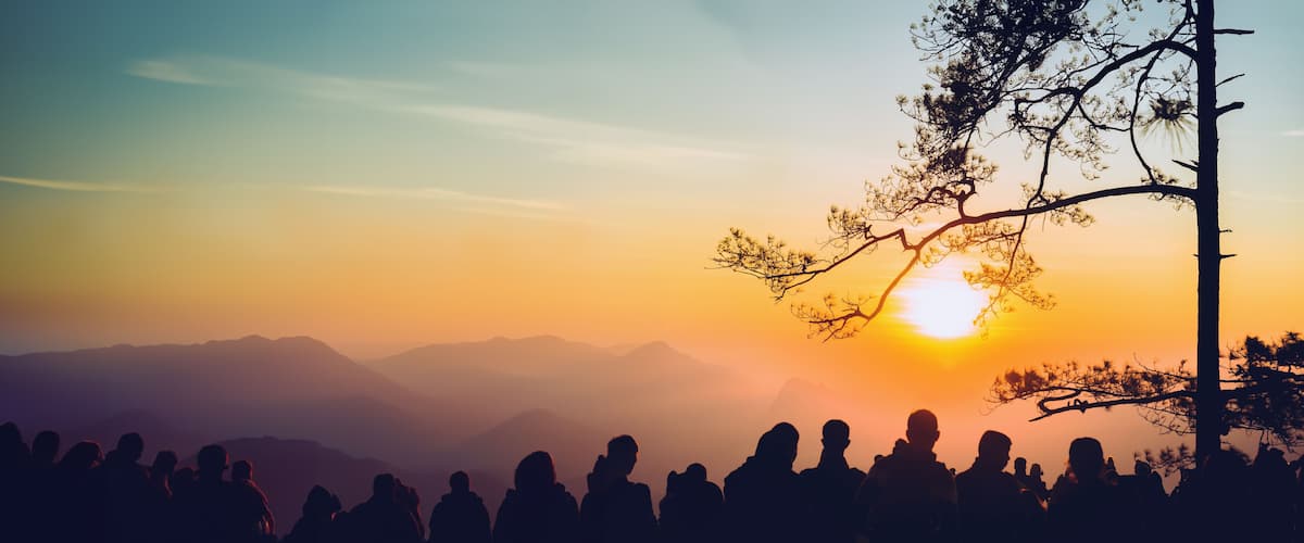 A silhouette of people at sunset with mountains in the background.