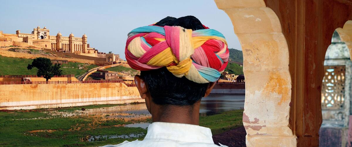 A person with a colorful turban, a historic fort, and a river.