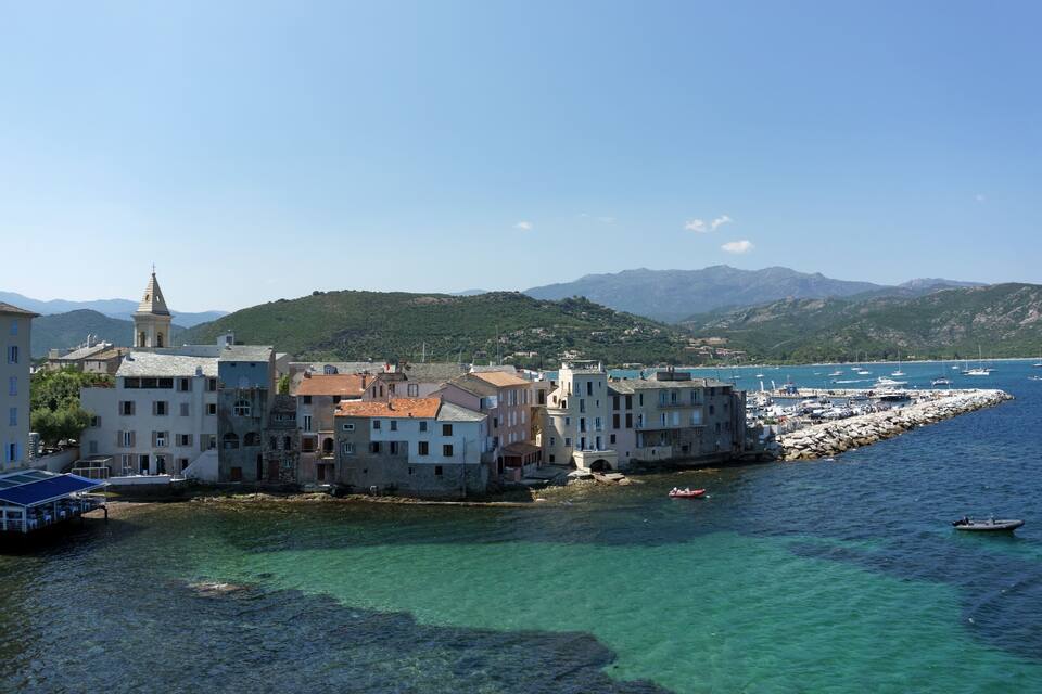 A coastal town with buildings along the water, boats, and mountains in the background.