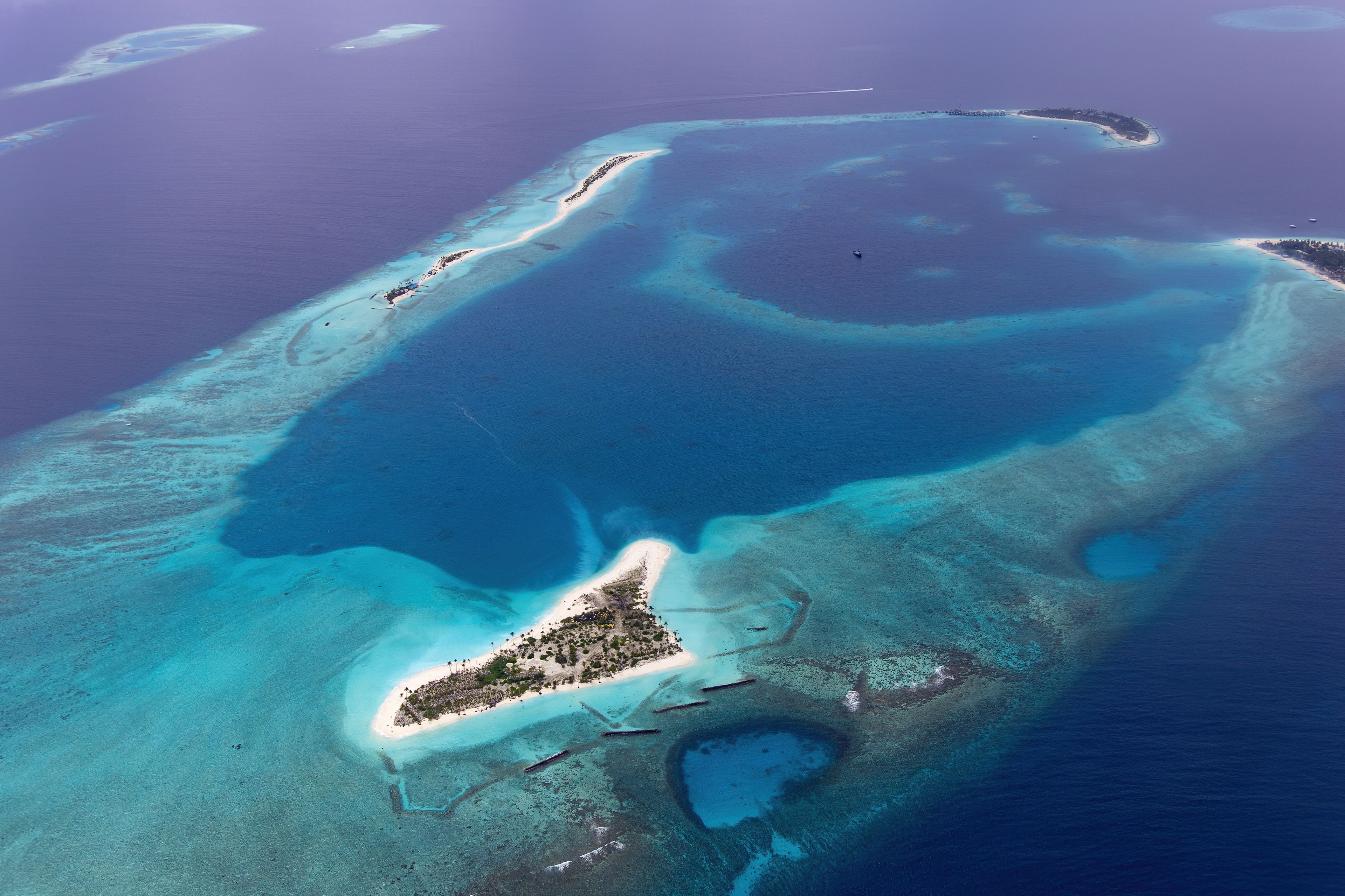 An aerial view of a tropical island with clear blue waters, a sandy beach, and a small settlement.