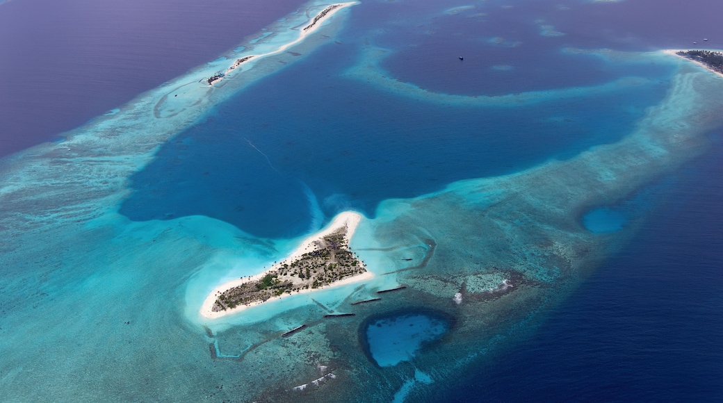 An aerial view of a tropical island with clear blue waters, a sandy beach, and a small settlement.