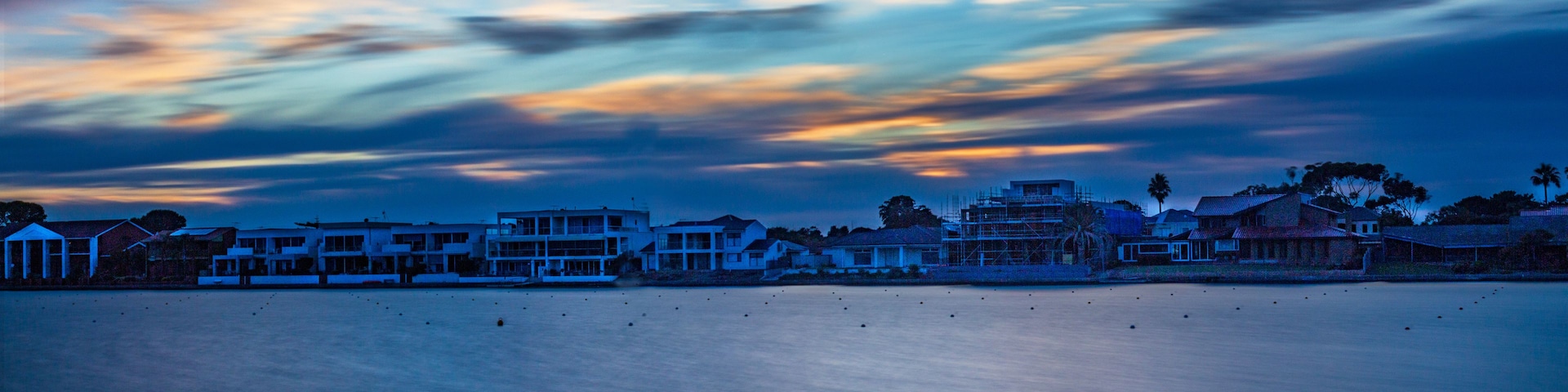 Un pueblo costero al anochecer, con edificios modernos y un mar tranquilo.