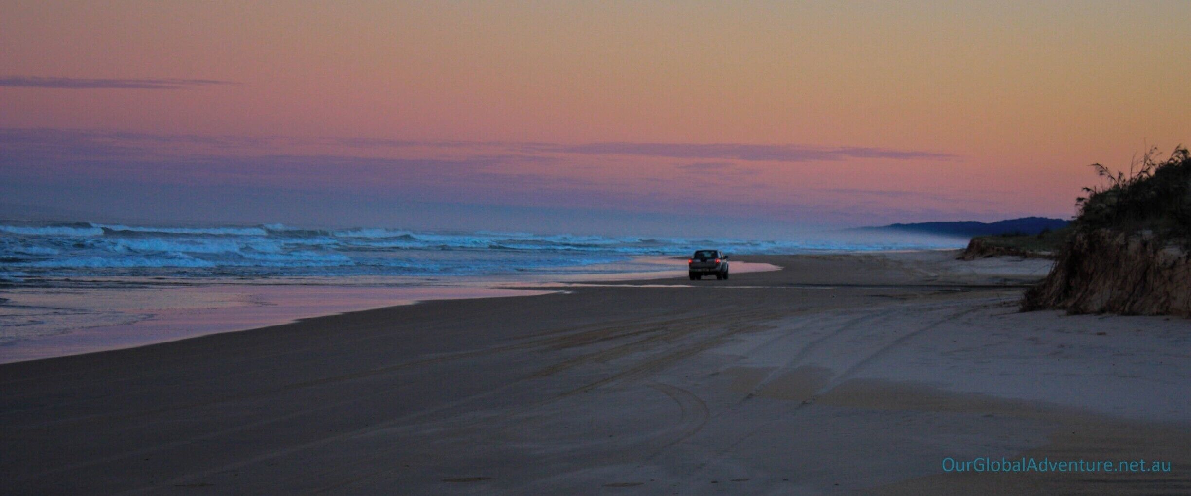 A beach with a vehicle on the sand near the water.