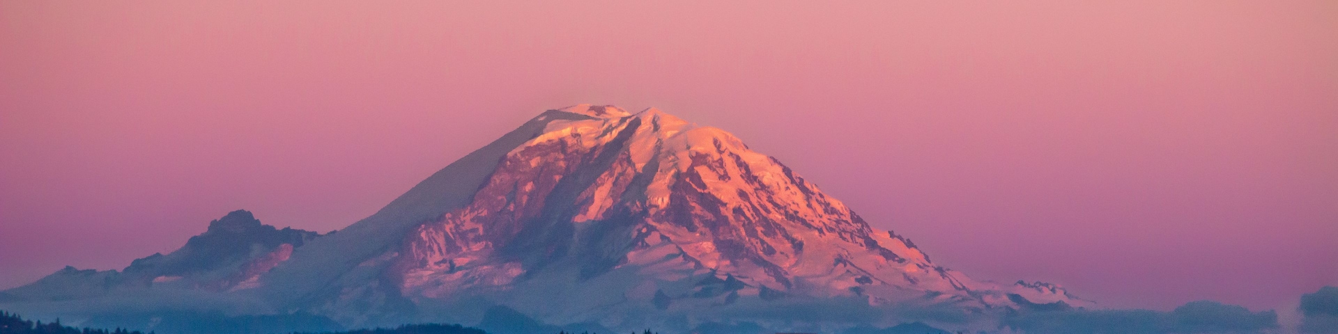 Montanha coberta de neve ao pôr do sol, com uma cidade em primeiro plano.
