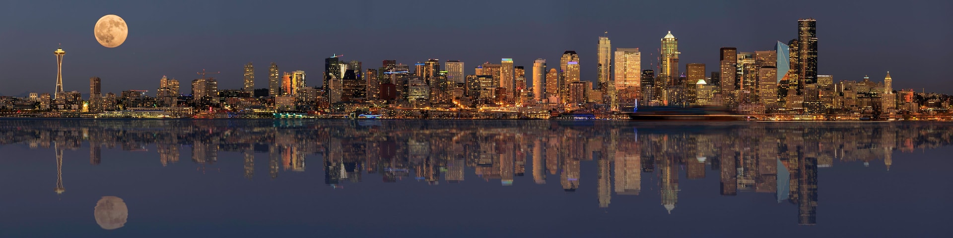 Un horizonte urbano nocturno con una luna llena en el cielo y su reflejo en el agua.