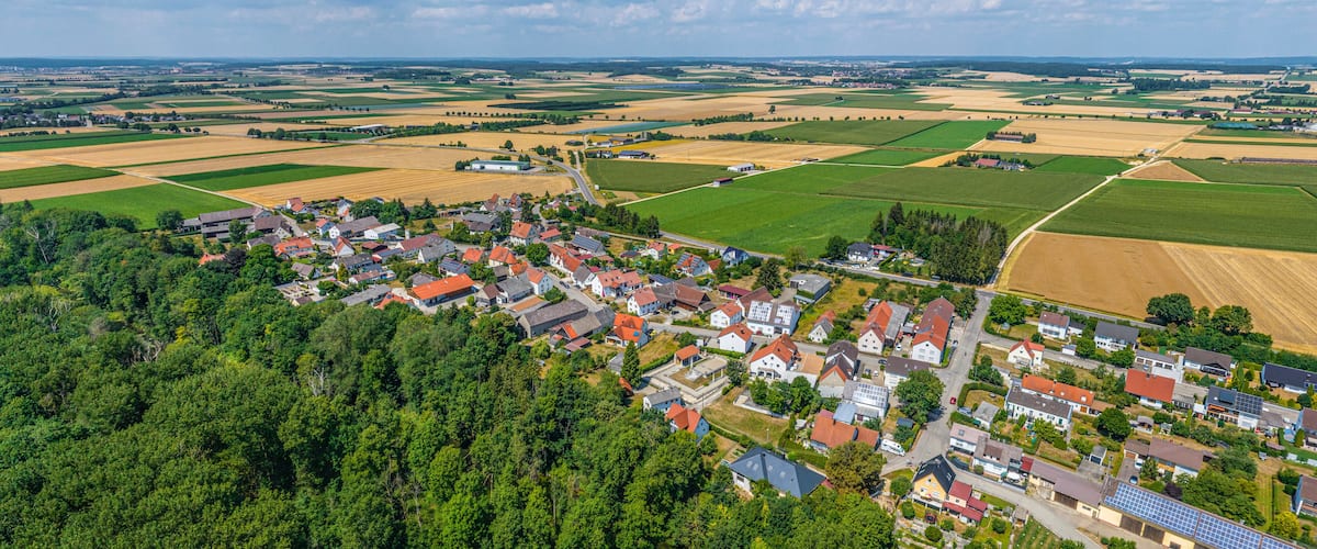 An aerial view of a rural village with houses, fields, and a forested area.