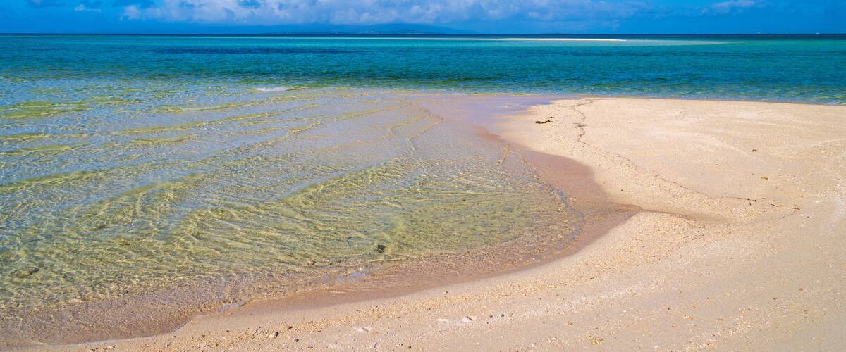 A beach with clear shallow waters and a sandy shore.